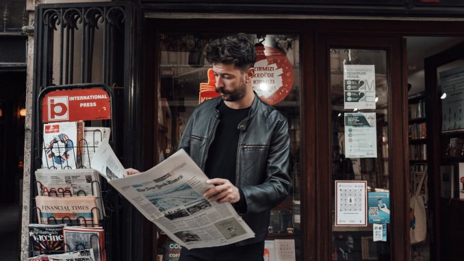 focused man reading newspaper on street