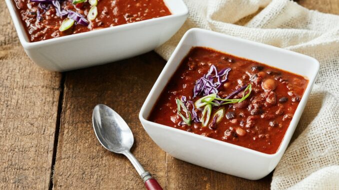 two bowls of chili and a spoon on a wooden table