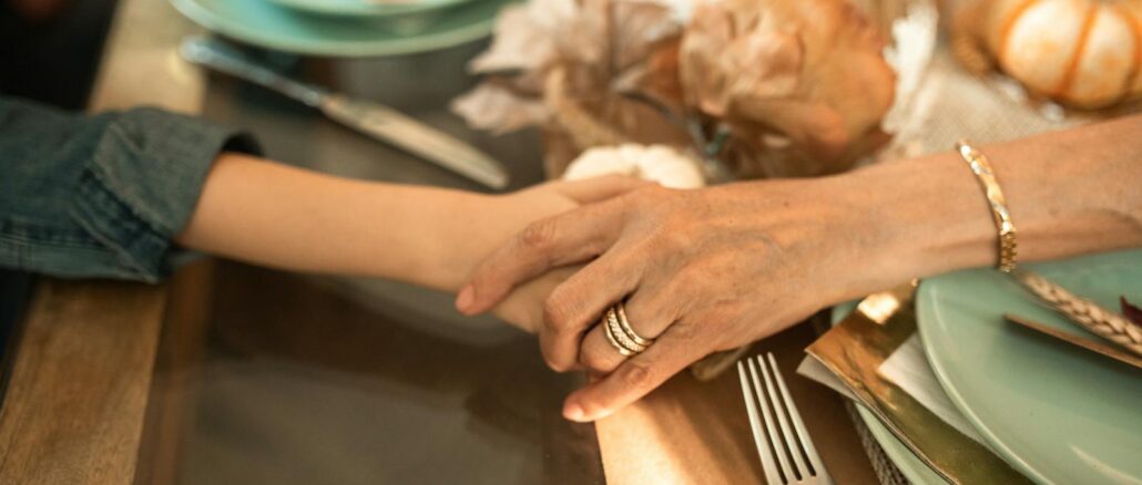 Close-up of an intergenerational handhold at a cozy Thanksgiving dinner table.