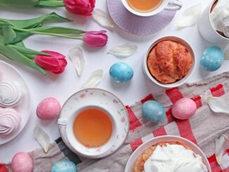 Colorful Easter tea party setup with tulips, pastries, and decorated eggs on a white table.