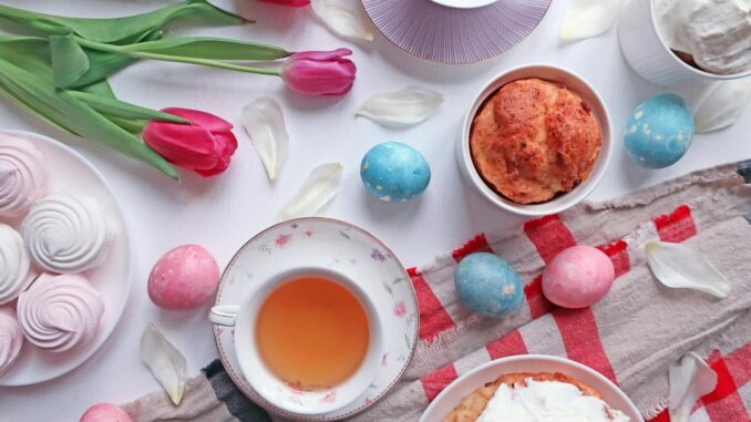 Colorful Easter tea party setup with tulips, pastries, and decorated eggs on a white table.